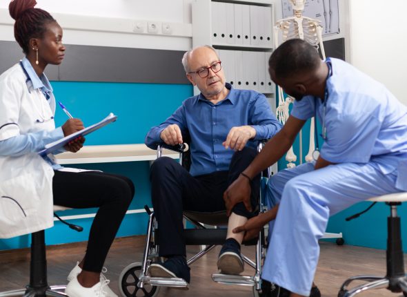 African american man nurse checking injured knee leg of sick senior patient